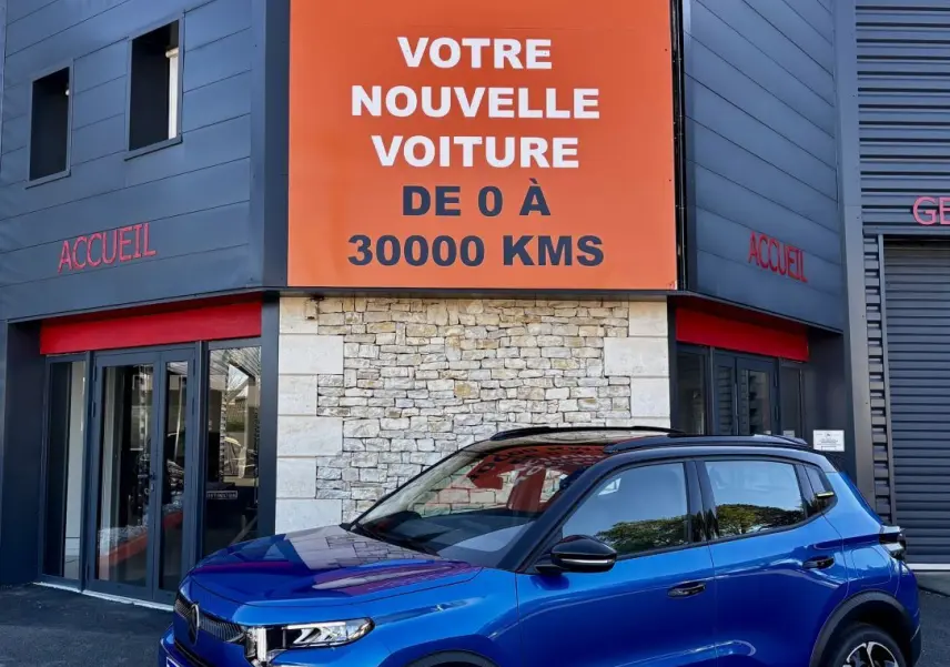 Citroën C3 100 BVM PLUS bleu vue 3/4 avant avec toit noir et jantes distinctives, devant un bâtiment commercial.