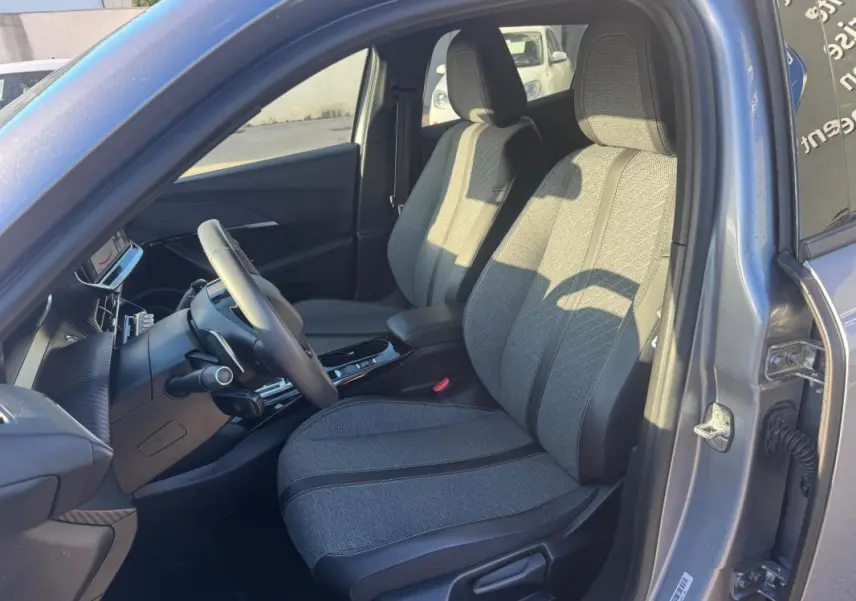 Intérieur avant droit du Peugeot 2008 Hybrid gris 2024, sièges tissu gris avec console centrale et volant visible.