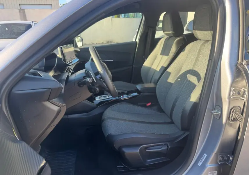 Intérieur avant droit du Peugeot 2008 Hybrid gris 2024, sièges tissu, tableau de bord avec écran tactile et volant.
