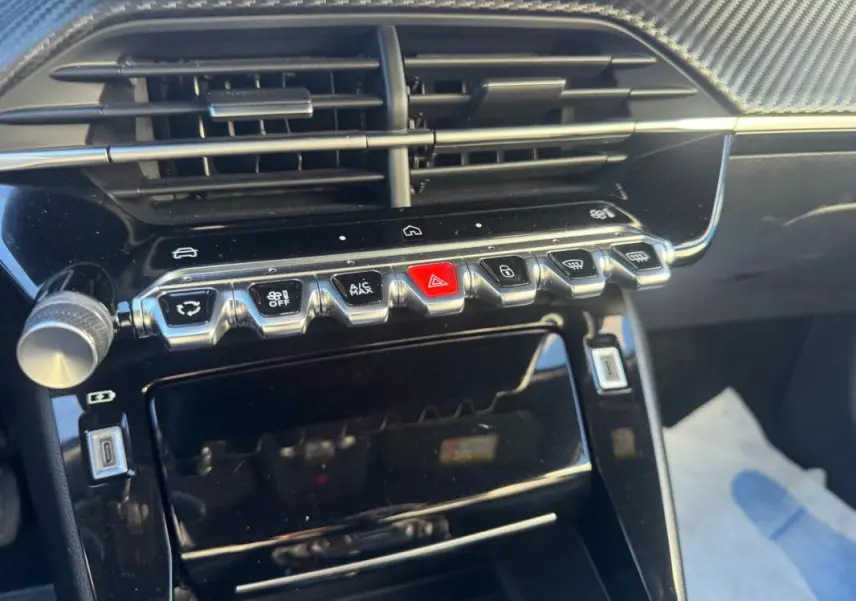 Vue rapprochée de la console centrale noire brillante du Peugeot 2008 Hybrid 136 avec boutons de commande et prise USB.