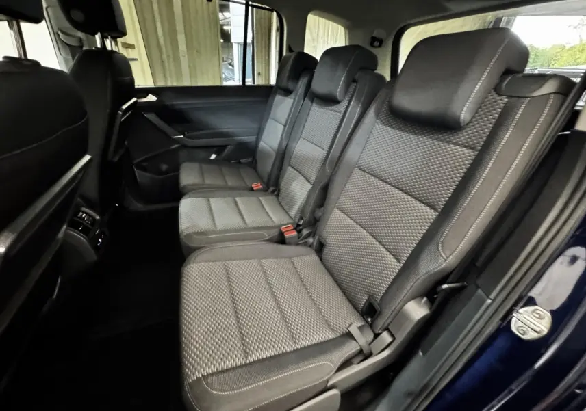 Vue intérieure côté droit sur la deuxième rangée de sièges gris du Volkswagen Touran bleu 2024, version 7 places.