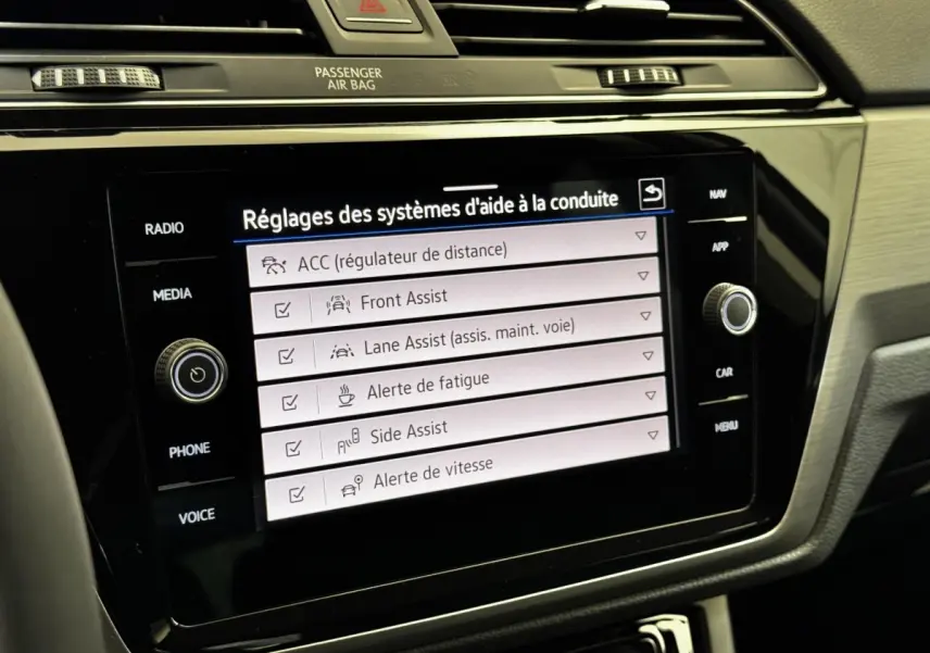 Écran tactile central du Volkswagen Touran 2024 affichant les réglages des aides à la conduite, intérieur noir.