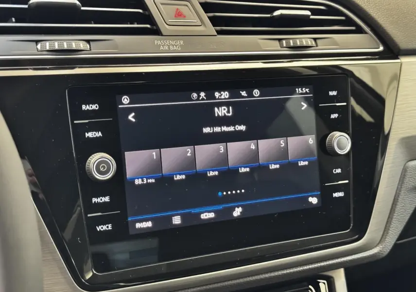 Gros plan sur l’écran tactile central noir du tableau de bord du Volkswagen Touran 2024 affichant la radio NRJ.