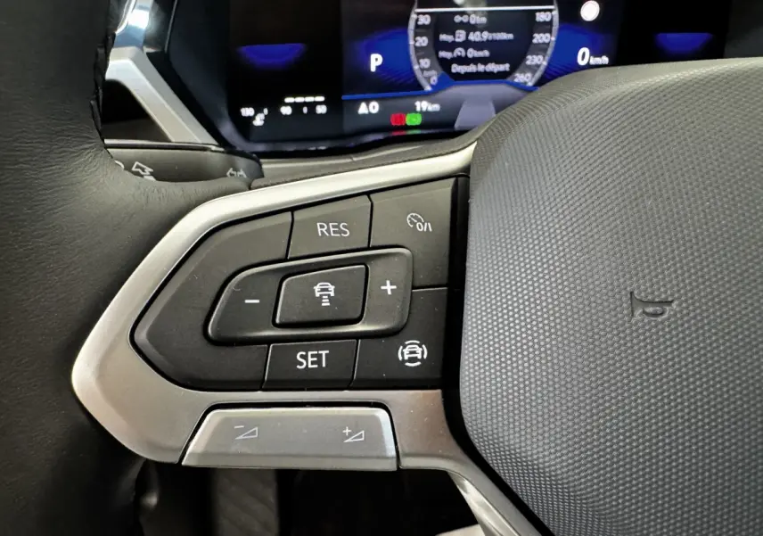 Gros plan sur le volant multifonctions du Volkswagen Touran 2024, boutons de régulateur de vitesse visibles, intérieur noir.