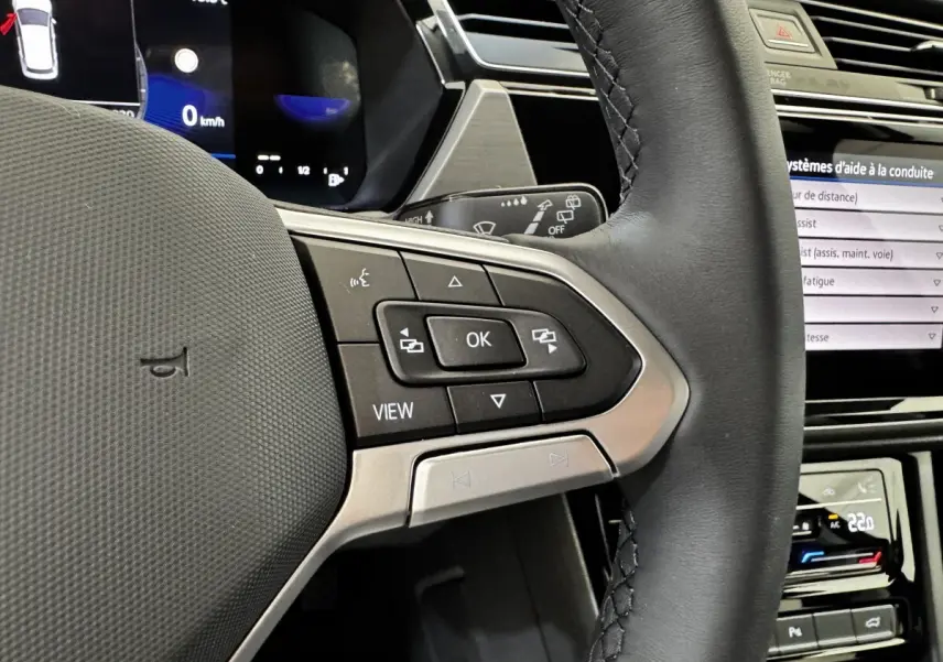 Gros plan sur le volant cuir noir côté gauche du Volkswagen Touran 2024 avec commandes multifonctions et tableau de bord digital.