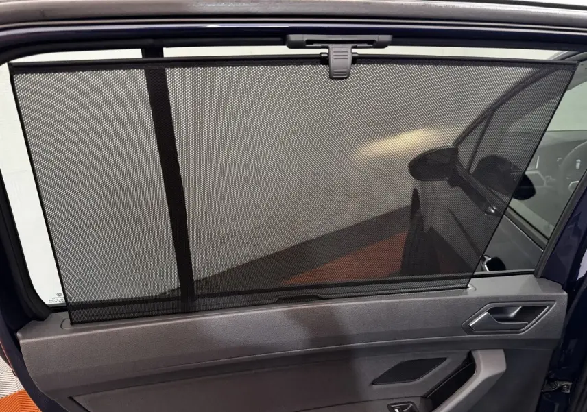 Vue intérieure de la porte arrière droite d’un Volkswagen Touran bleu 2024 avec pare-soleil en filet déployé.