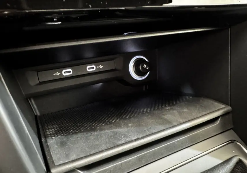 Gros plan sur la console centrale noire du Volkswagen Touran 2024, montrant prises USB et prise 12V éclairée.