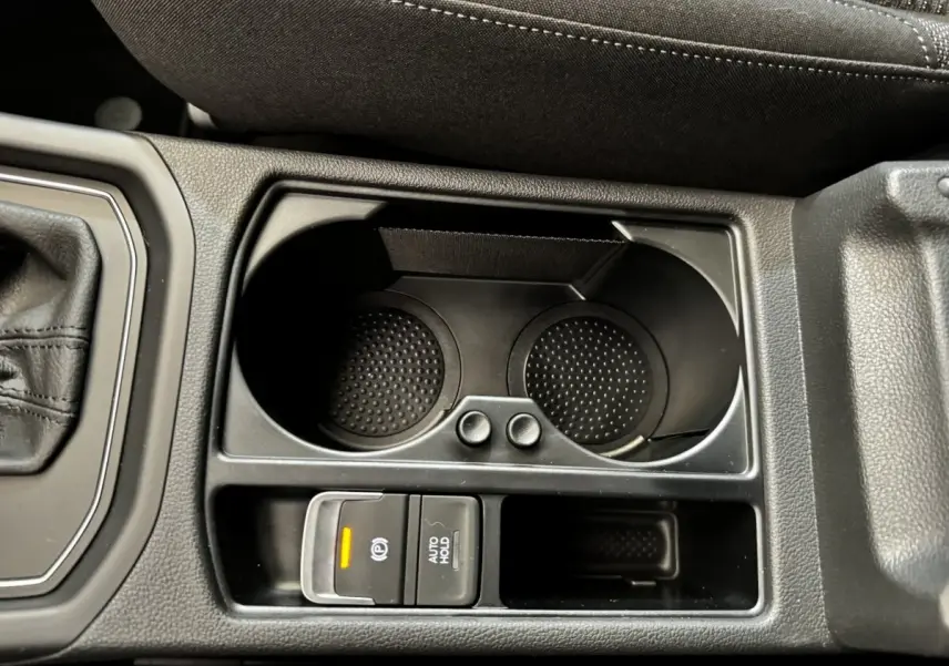 Gros plan sur la console centrale noire du Volkswagen Touran 2024, avec porte-gobelets et commandes frein à main électrique.