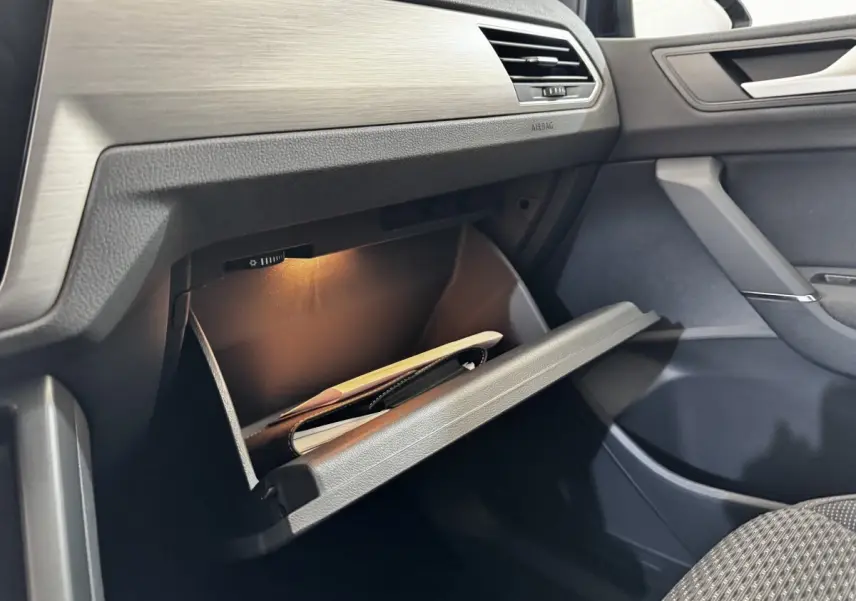Vue intérieure côté passager du Volkswagen Touran 2024 avec boîte à gants ouverte et éclairage intérieur allumé.