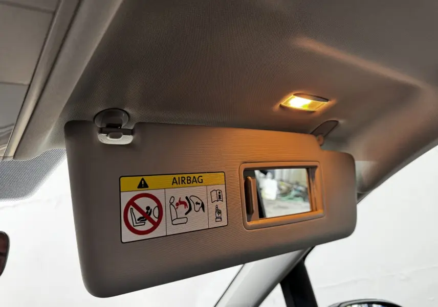Vue intérieure du pare-soleil côté conducteur du Volkswagen Touran 2024 bleu avec miroir et avertissement airbag éclairé.