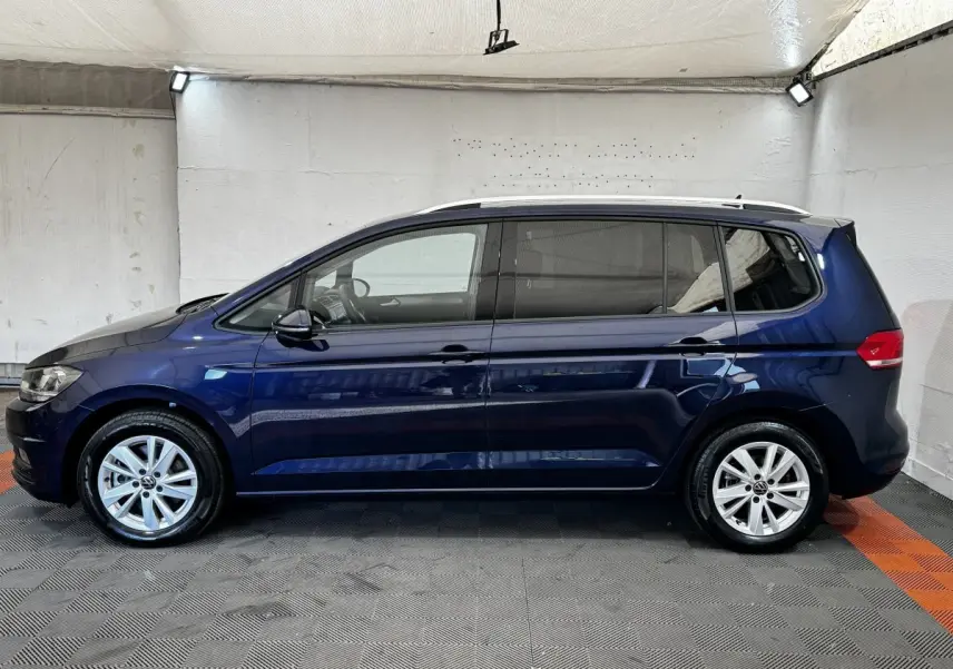 Profil latéral droit d'un Volkswagen Touran bleu 2024 avec jantes alliage et toit ouvrant visible en intérieur neutre.