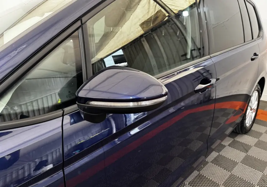 Vue rapprochée du côté gauche d’un Volkswagen Touran bleu 2024, mettant en valeur le rétroviseur avec clignotant intégré.