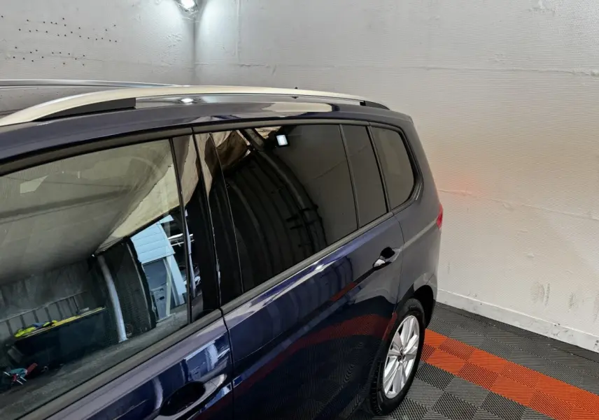 Vue latérale droite du Volkswagen Touran bleu 2024, mettant en valeur les vitres teintées et les barres de toit chromées.