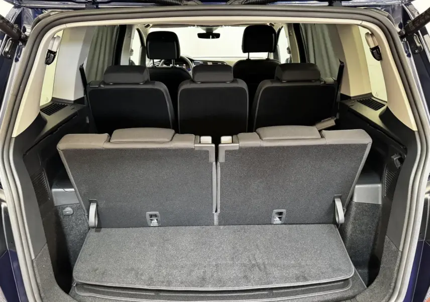 Vue arrière du coffre ouvert d’un Volkswagen Touran bleu 2024, montrant la troisième rangée de sièges relevée.