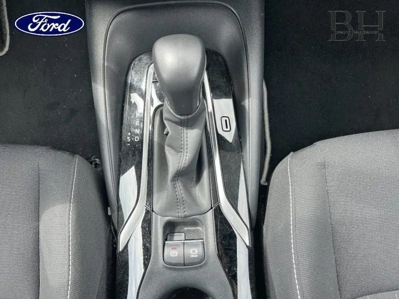 Le levier de vitesses automatique noir avec coutures grises, entouré de garnitures brillantes, entre deux sièges gris.