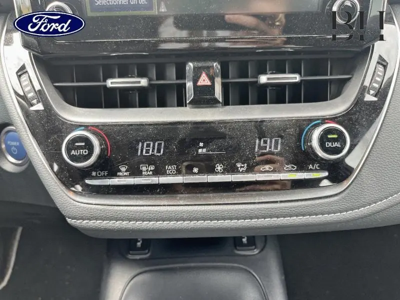 Panneau de climatisation automatique bi-zone noir avec affichage digital dans une Toyota Corolla blanche vue de face.