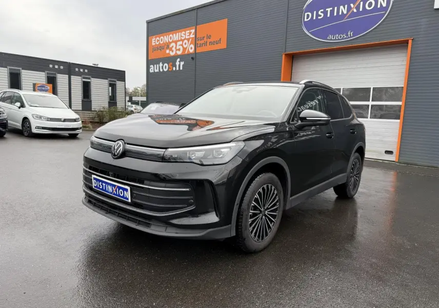 Volkswagen Tiguan noir grenadille métallisé vu en 3/4 avant droit sur parking devant un bâtiment commercial.