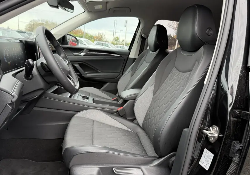 Vue intérieure côté conducteur du Volkswagen Tiguan 2025 noir grenadille, sièges tissu et cuir gris, tableau de bord digital.