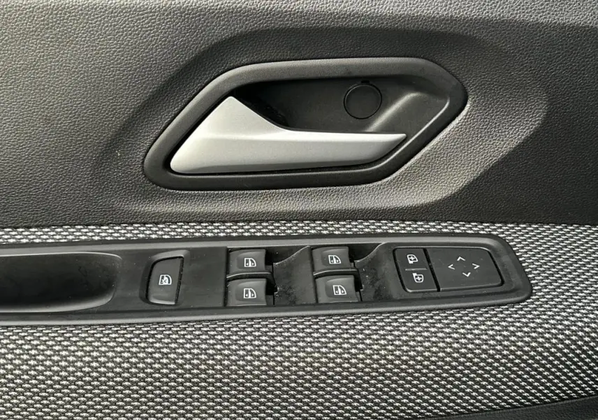 Gros plan sur la poignée intérieure et les commandes des vitres côté conducteur d'une Dacia Sandero blanche 2024.