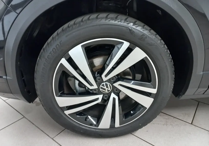Gros plan sur la roue avant gauche du Volkswagen T-Roc noir intense, mettant en valeur la jante alliage bicolore au design dynamique.