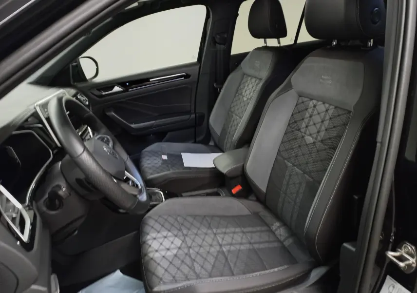 Vue intérieure côté conducteur du Volkswagen T-Roc 1.5 TSI R-Line 2025, sièges en tissu noir à motifs géométriques.