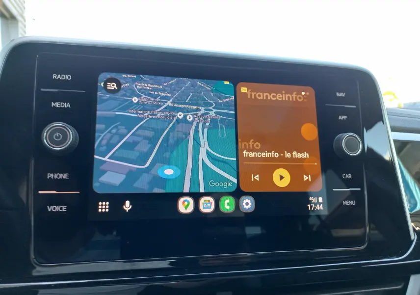 Écran central tactile du Volkswagen T-Roc 2025 affichant navigation et radio, avec commandes latérales visibles.