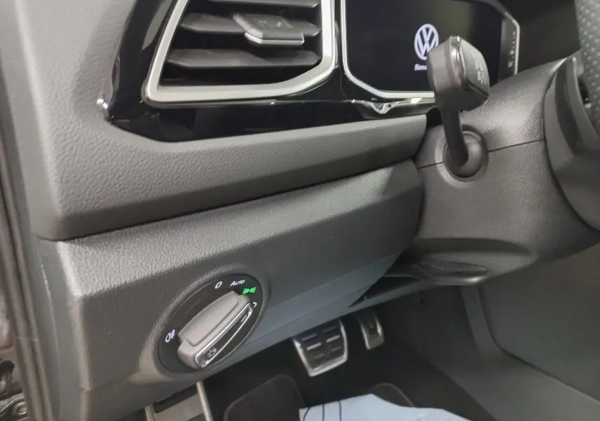 Détail intérieur côté gauche du tableau de bord du Volkswagen T-Roc 2025 avec commandes d'éclairage et aérateurs noirs.