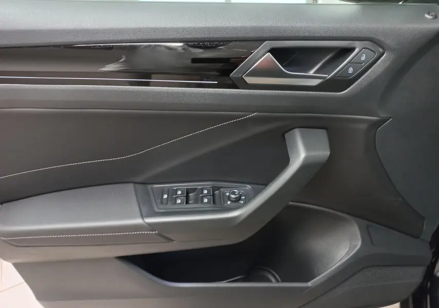 Vue rapprochée de la porte avant gauche du Volkswagen T-Roc 2025 noir intense, avec commandes électriques et garniture noire élégante.