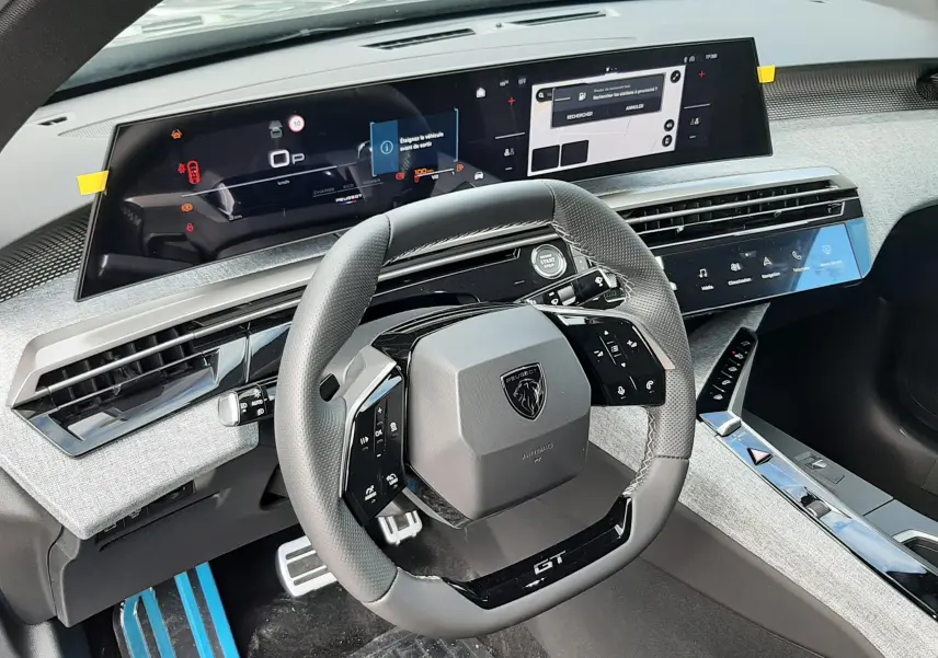 Vue intérieure du poste de conduite du Peugeot 3008 Hybrid 2026, avec volant compact GT, tableau de bord numérique et finition tissu gris clair.