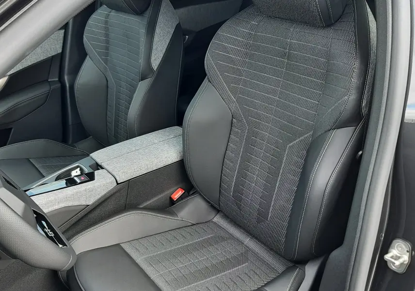 Vue intérieure rapprochée des sièges avant du Peugeot 3008 gris titane, avec sellerie mixte tissu et cuir noir et logo brodé sur appuie-tête.