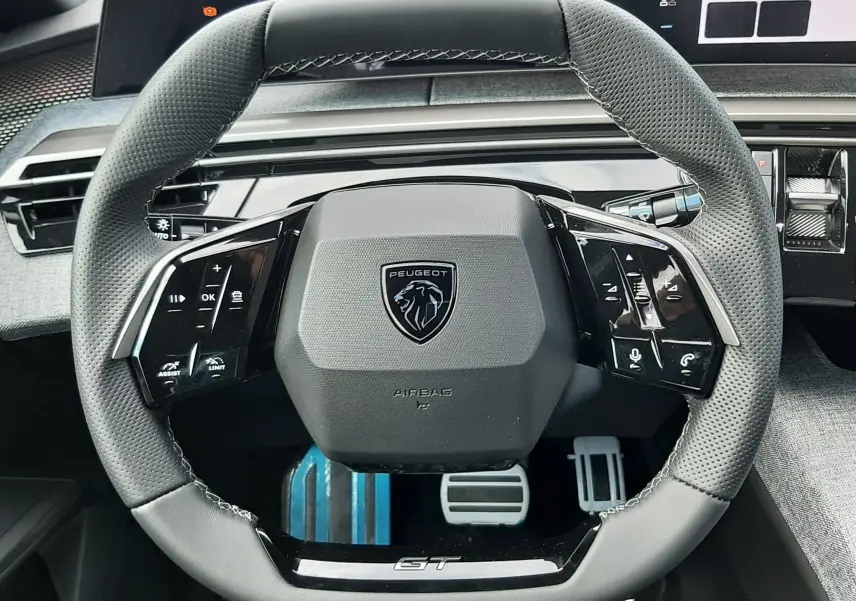Vue rapprochée du volant GT du Peugeot 3008 hybride 2026, avec commandes intégrées et tableau de bord numérique en arrière-plan.