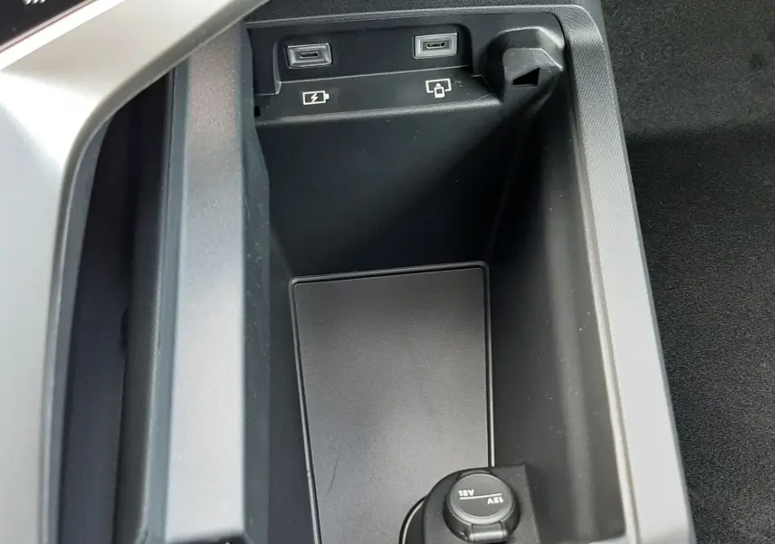 Gros plan sur la console centrale noire du Peugeot 3008 1.2 Hybrid, montrant prises USB et prise 12V.