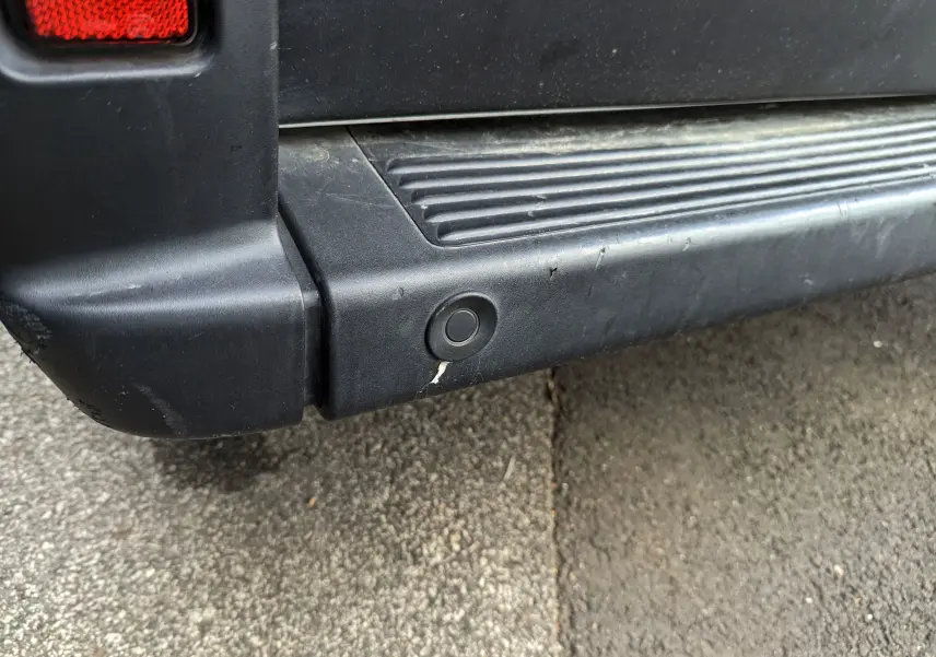 Gros plan sur le pare-chocs arrière noir du Fiat Ducato Fourgon blanc, montrant un capteur de recul circulaire.