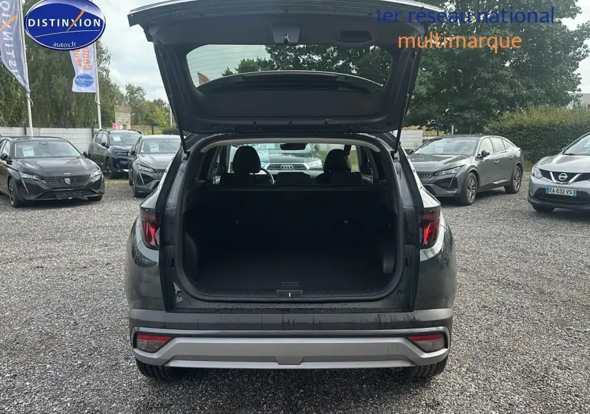 Vue arrière d'un Hyundai Tucson vert cyprès 2025 avec coffre ouvert sur un parking multimarque.