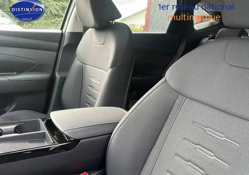 Gros plan sur les sièges avant gris du Hyundai Tucson 2025, mettant en valeur les surpiqûres et l'accoudoir central.