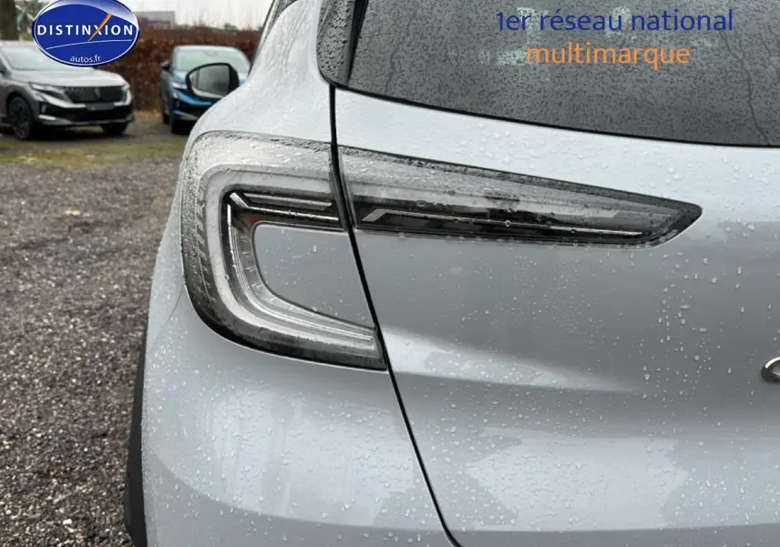 Gros plan sur le feu arrière gauche du Renault Captur gris rafale 2026 sous la pluie, avec logo partiel visible.