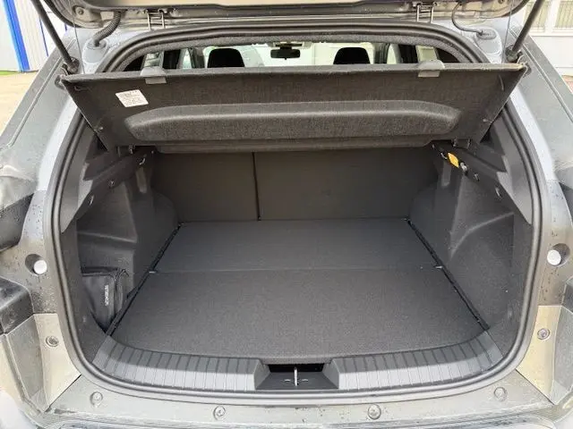 Coffre ouvert vu de l'arrière d'un Dacia Duster 1.8 Hybrid 155 Journey gris schiste avec sellerie spécifique et prise 12V.