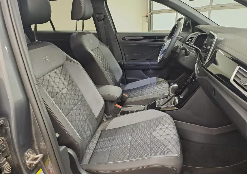 Vue intérieure côté conducteur du Volkswagen T-Roc 1.5 TSI R-Line 2025, sièges tissu et alcantara gris avec surpiqûres.