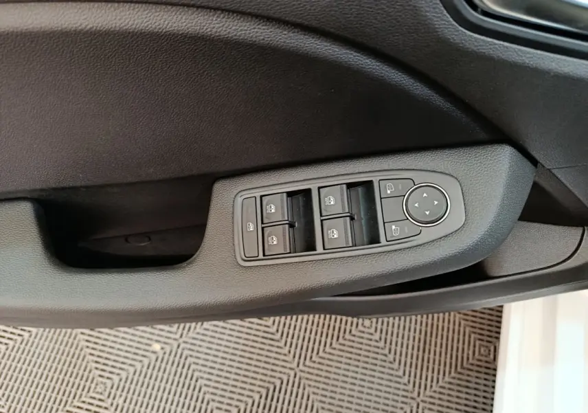 Vue rapprochée de la commande des vitres électriques et rétroviseurs sur la porte côté conducteur d'une Renault Clio blanche 2024.