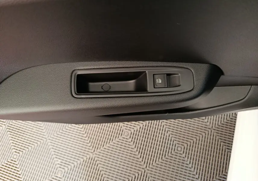 Détail de la commande de verrouillage des portes sur la portière intérieure noire d'une Renault Clio blanche.