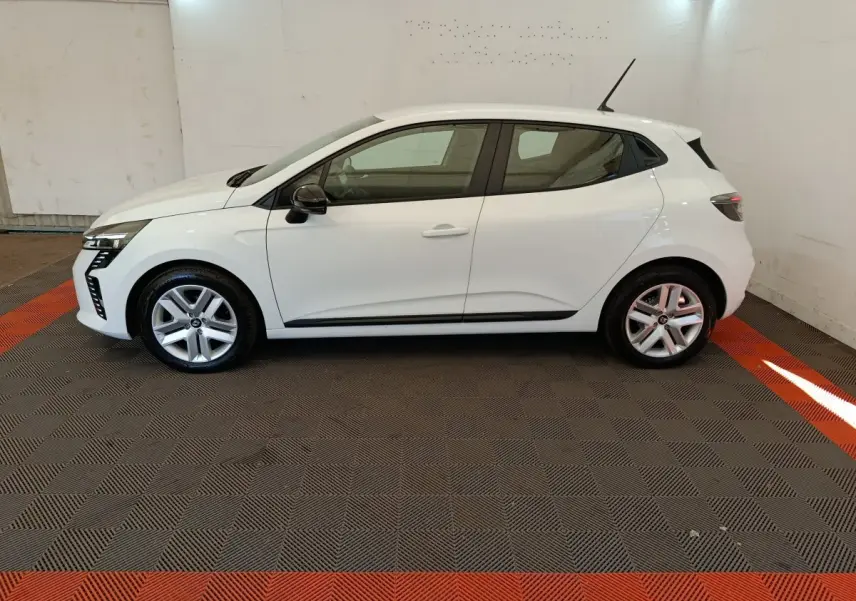 Profil droit d'une Renault Clio blanche 2024 garée en intérieur sur un sol à damiers gris et rouge.