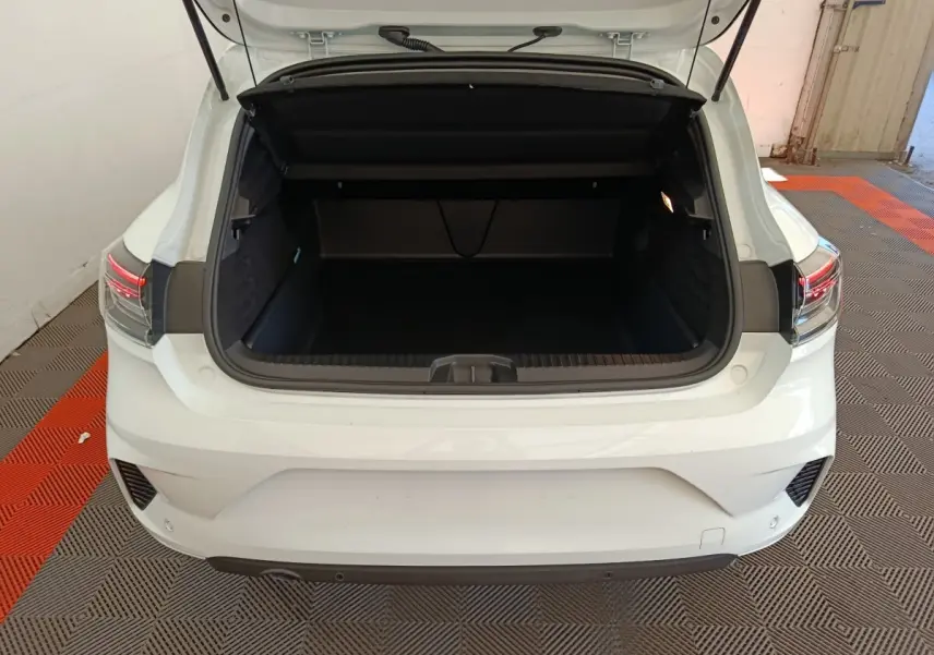 Vue arrière d'une Renault Clio blanche 2024 avec coffre ouvert, feux arrière LED et capteurs de stationnement visibles.