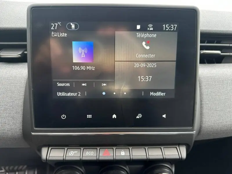 Écran tactile central de la Renault Clio 2025 affichant la radio et la connexion téléphone, avec boutons de commande en dessous.