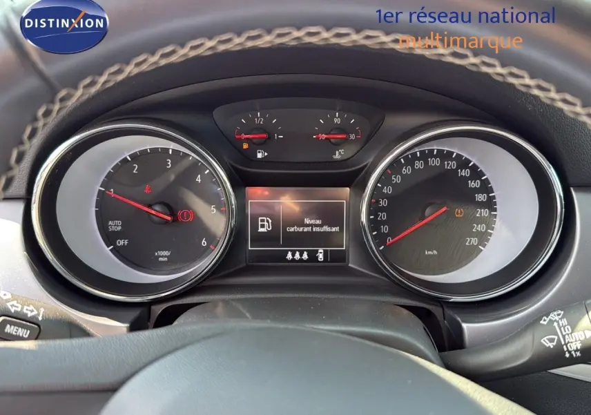 Vue rapprochée du tableau de bord de l'Opel Astra Sports Tourer gris minéral, affichant un avertissement de carburant faible.