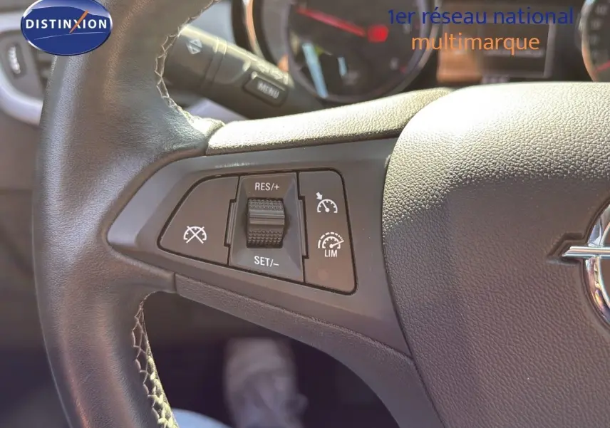 Gros plan sur les commandes de régulateur de vitesse au volant en cuir noir de l'Opel Astra Sports Tourer gris minéral.