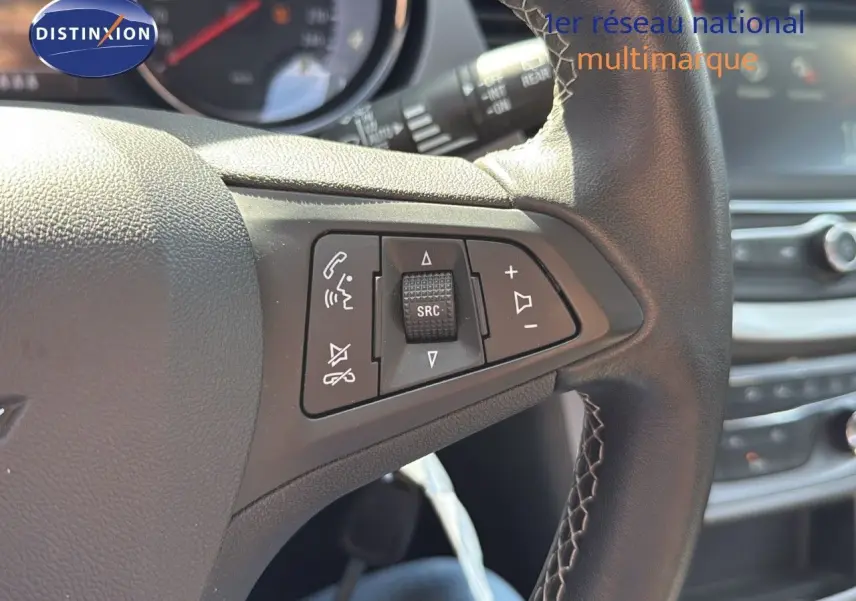 Gros plan sur les commandes au volant en cuir noir de l'Opel Astra Sports Tourer gris minéral, tableau de bord en arrière-plan.