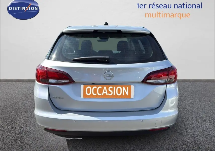 Vue arrière d'une Opel Astra Sports Tourer gris minéral métal avec feux rouges et plaque "OCCASION" visible.
