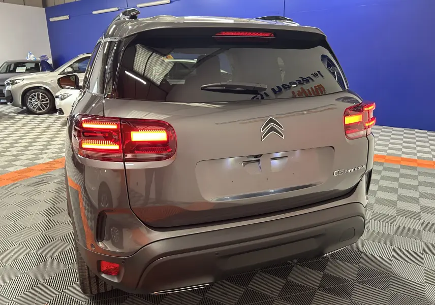 Vue 3/4 arrière d'un Citroën C5 Aircross gris platinium avec feux arrière allumés dans un showroom.