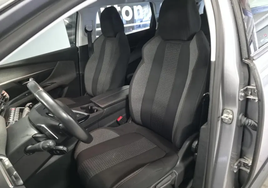 Vue intérieure côté conducteur du Peugeot 5008 gris 2020, sièges tissu bicolore avec accoudoir central ouvert.