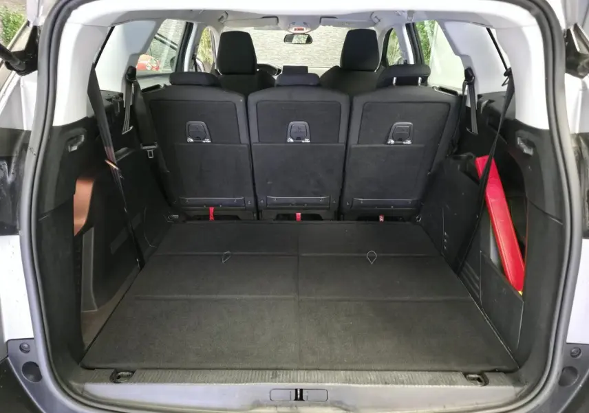 Coffre ouvert vu de l'arrière d'un Peugeot 5008 gris, sièges arrière relevés et plancher de coffre plat.